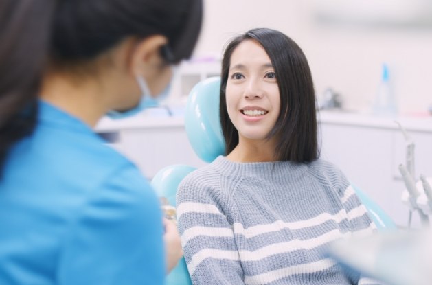 Young woman in gray sweater talking to dentist