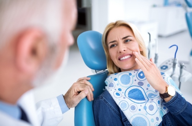 Woman holding her cheek in pain while talking to emergency dentist in Westfield