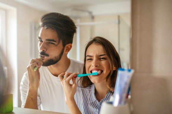 Couple smiling while brushing teeth in bathroom together