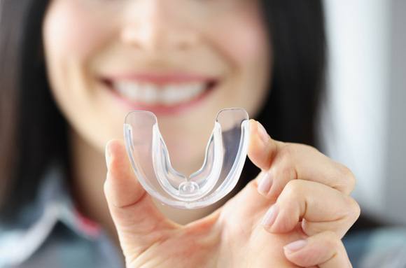Smiling woman holding clear mouthguard