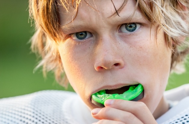 Young boy placing green athletic mouthguard over his teeth