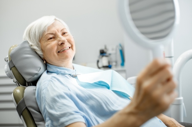 Senior dental patient admiring her smile in mirror after visiting Westfield prosthodontist