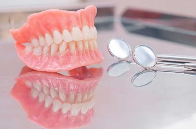 Set of full dentures on tray next to two dental mirrors