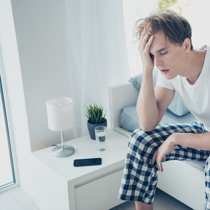 man sitting on edge of bed tired