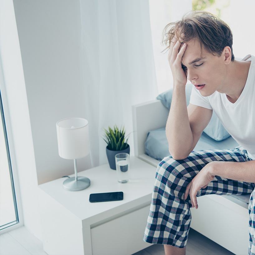 Man sitting on edge of bed holding his head in exhaustion