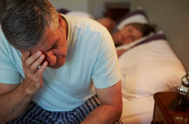 Man sitting on edge of bed rubbing his eyes