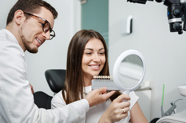 dentist helping smiling patient pick a shade of veneers