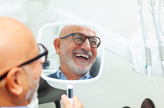 A senior man admiring his new smile with a hand mirror