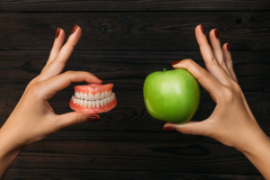 Left hand holding a pair of dentures and right hand holding an apple